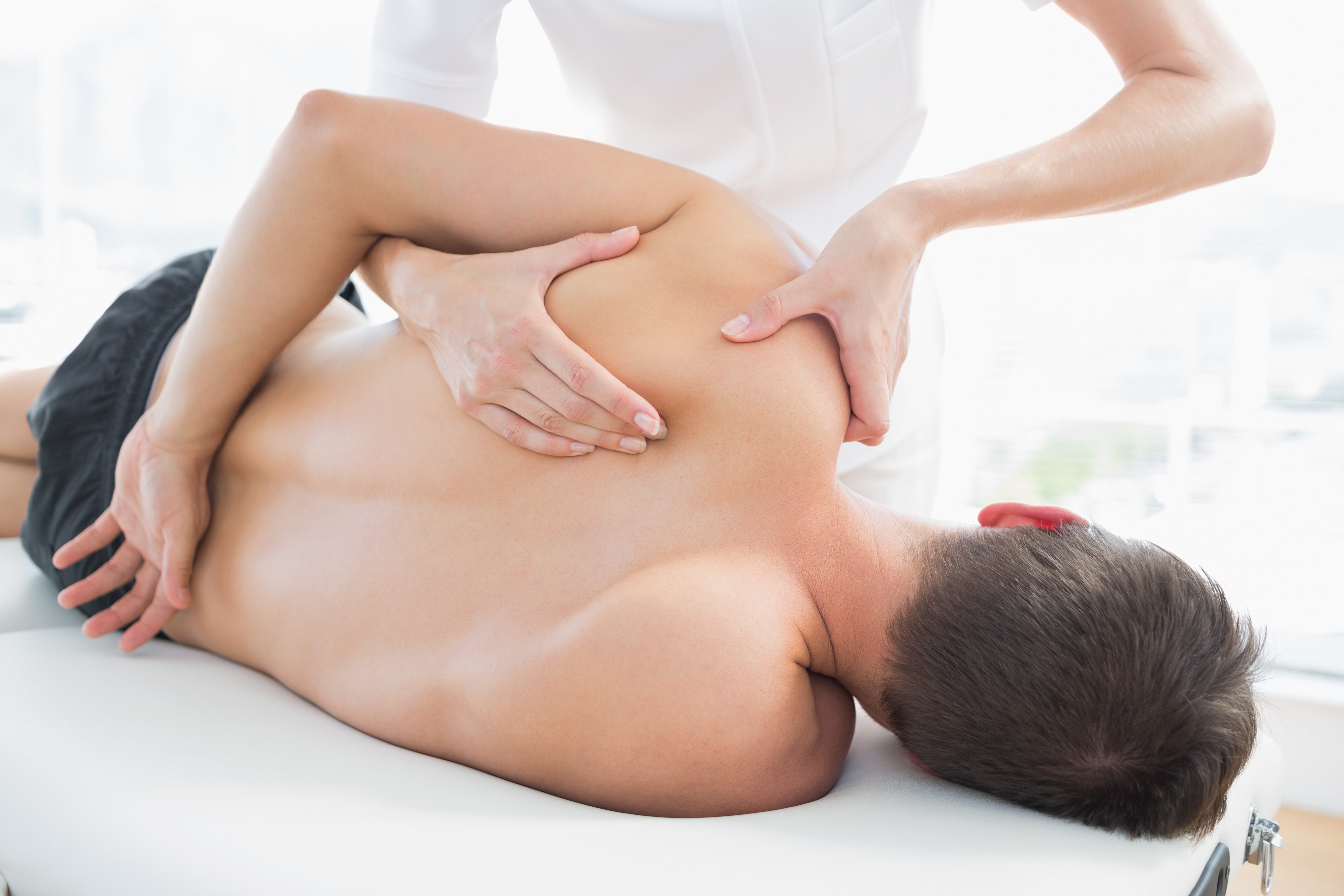 A man lying face down receiving a back and shoulder massage from a therapist