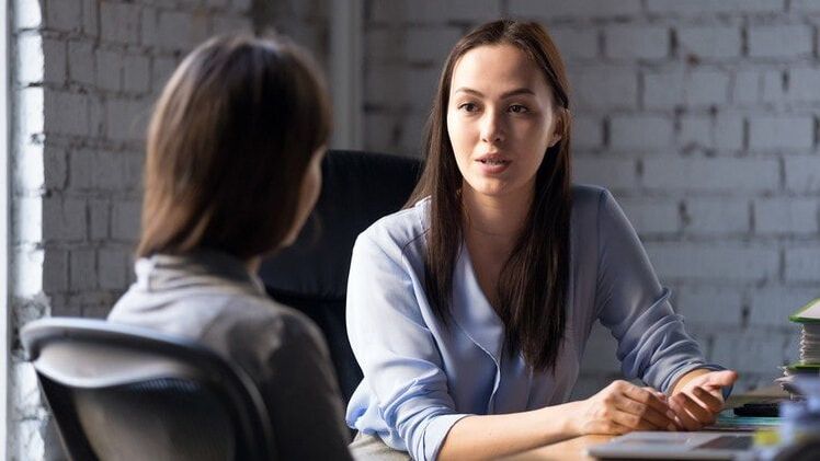 A woman in a light blue blouse speaking with a client across a desk