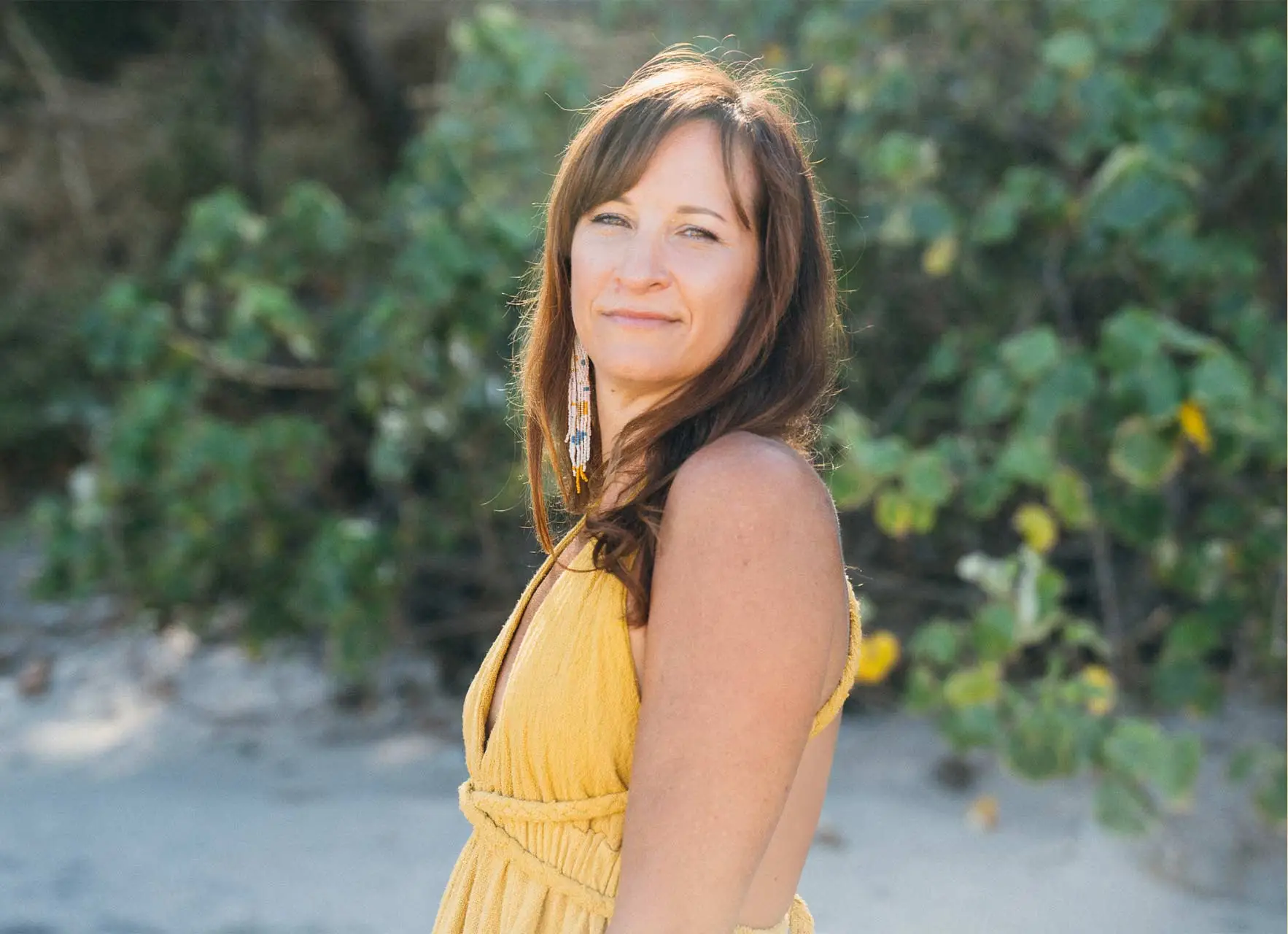 Beth Weinstein in a yellow halter dress smiling over her shoulder outdoors