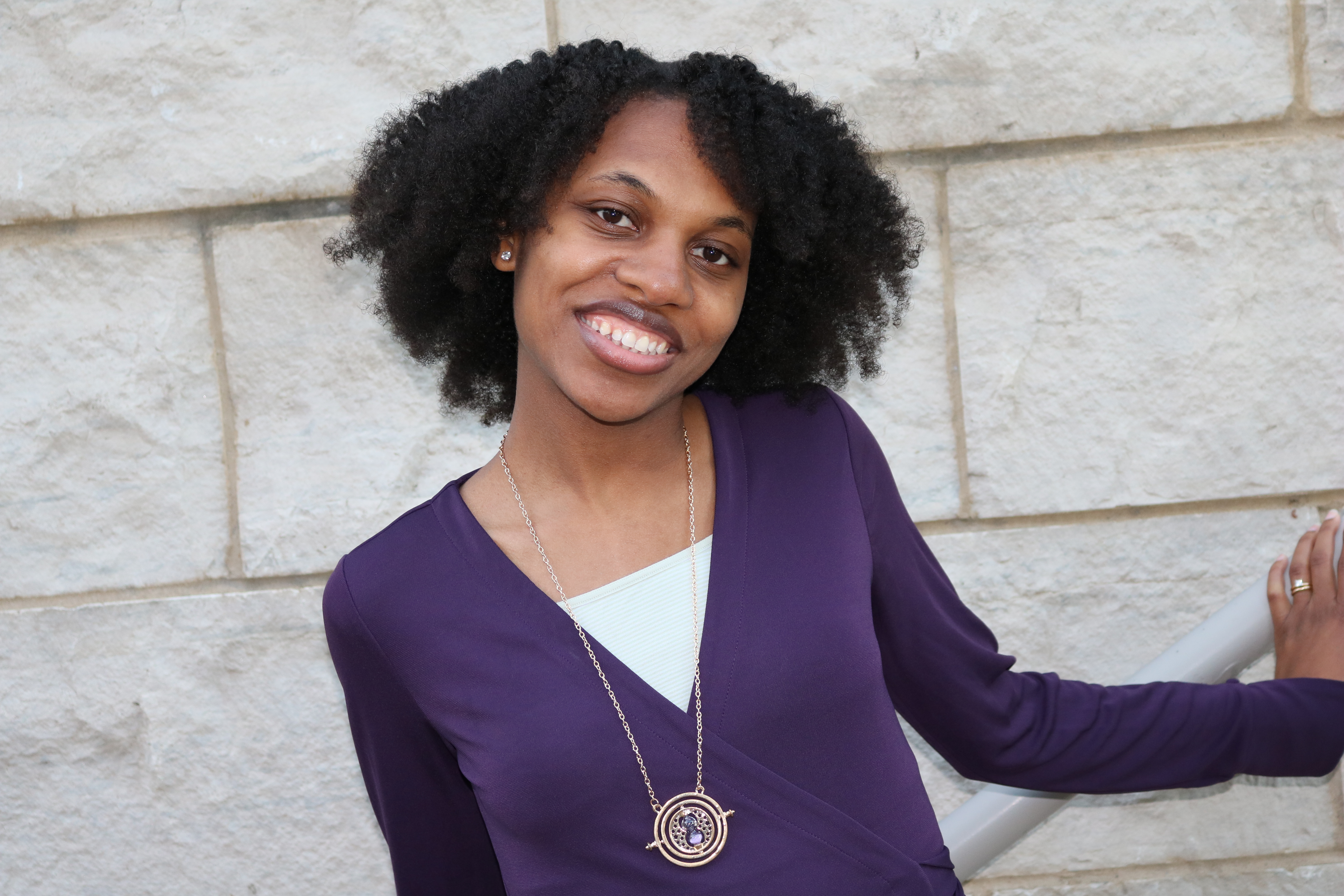 Dr. Lisa Battle-Gwathney, Ph.D., PCC, owner of Beyond Grand Coaching, LLC, smiling in a purple top against a stone wall.