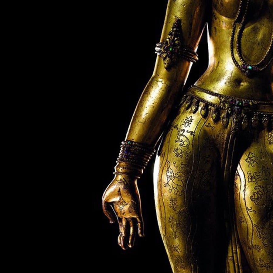 Close-up of a gilded bronze tantric goddess statue with jeweled adornments against a black background