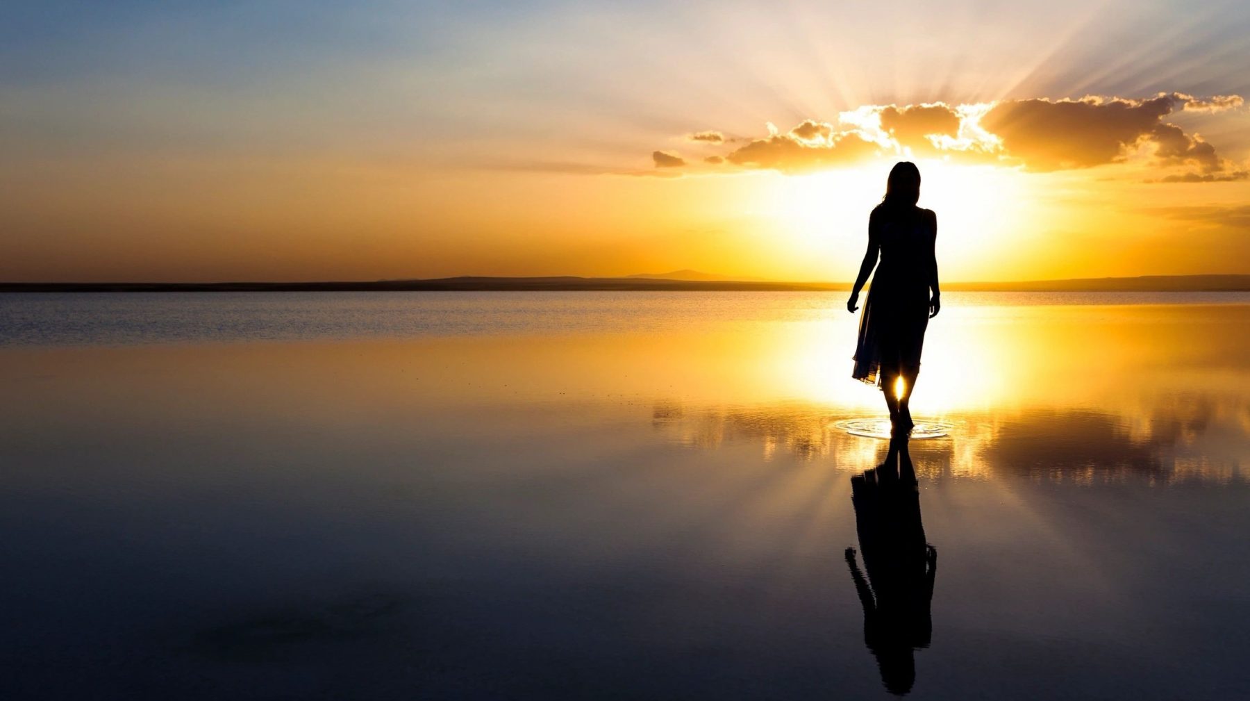 Silhouette of a woman standing in a reflective shallow lake at golden sunset