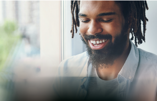 A person with dreadlocks smiling while looking down near a window