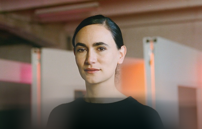 A leader with dark slicked-back hair in a black top against a warm, colorful background