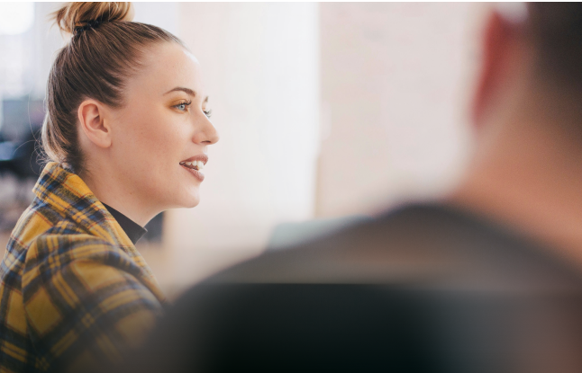 A person in a yellow plaid jacket smiling in profile in an office setting