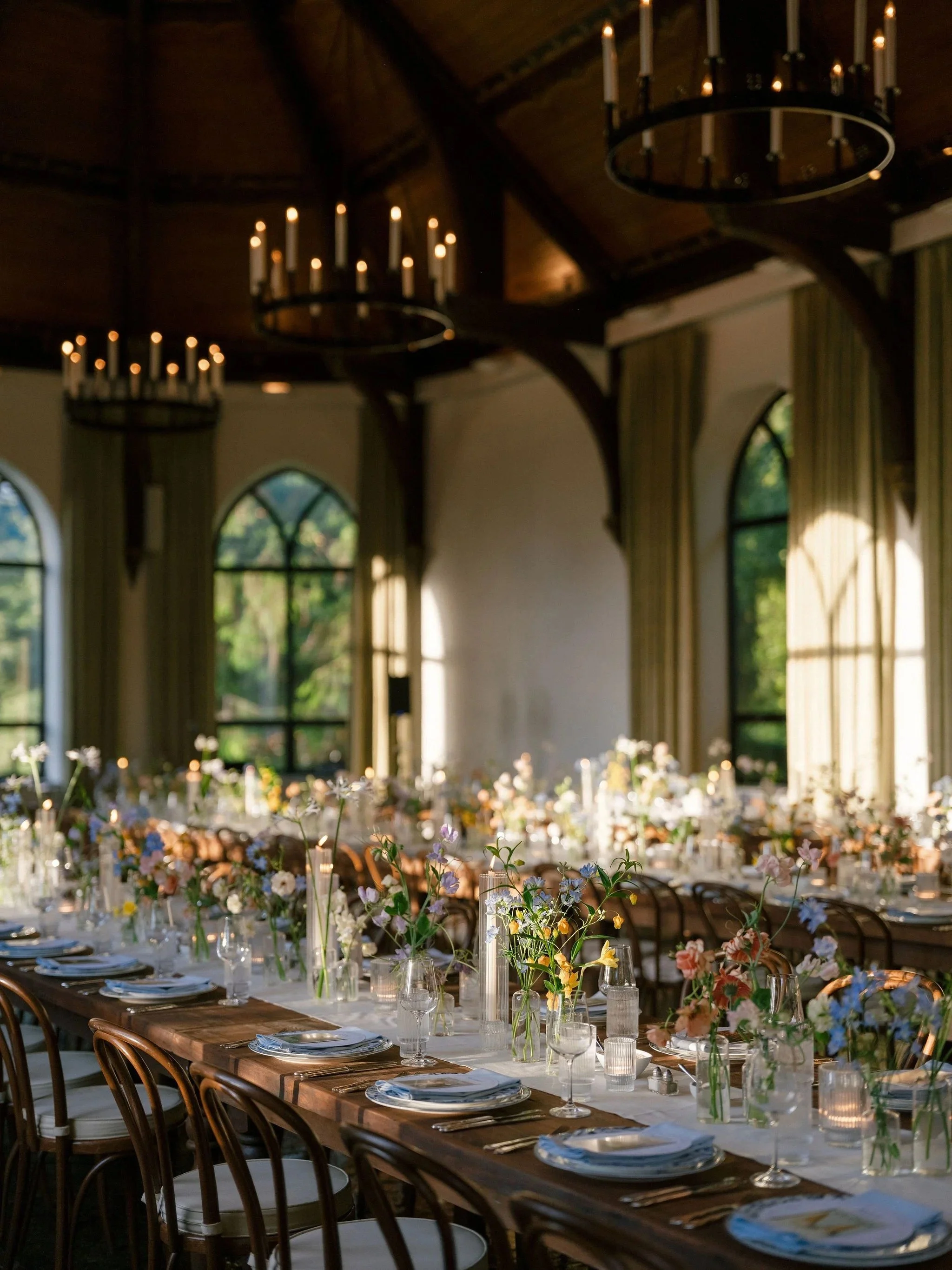 Colorful reception in a rustic hall with gothic arched windows and wildflower tables.