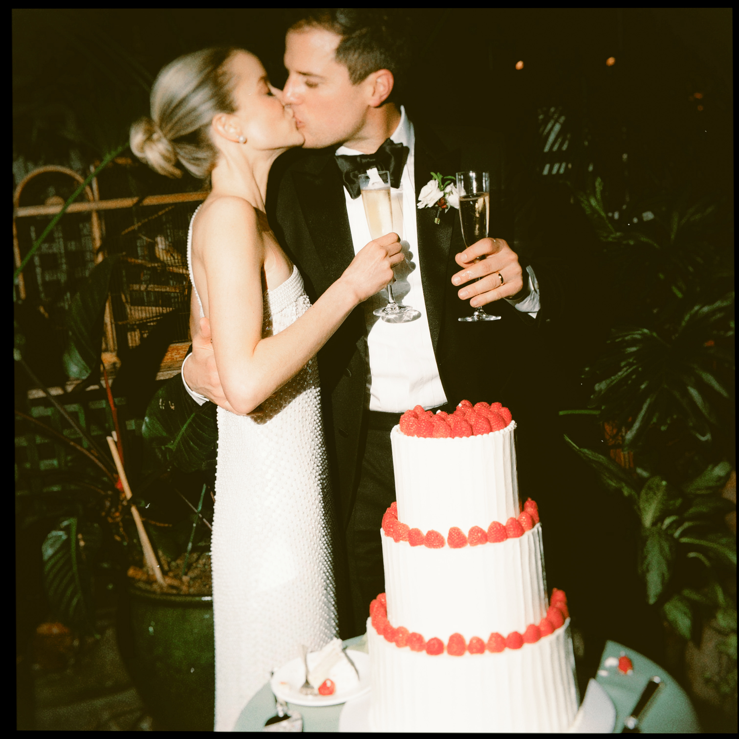 Couple kissing beside a three-tier strawberry wedding cake.