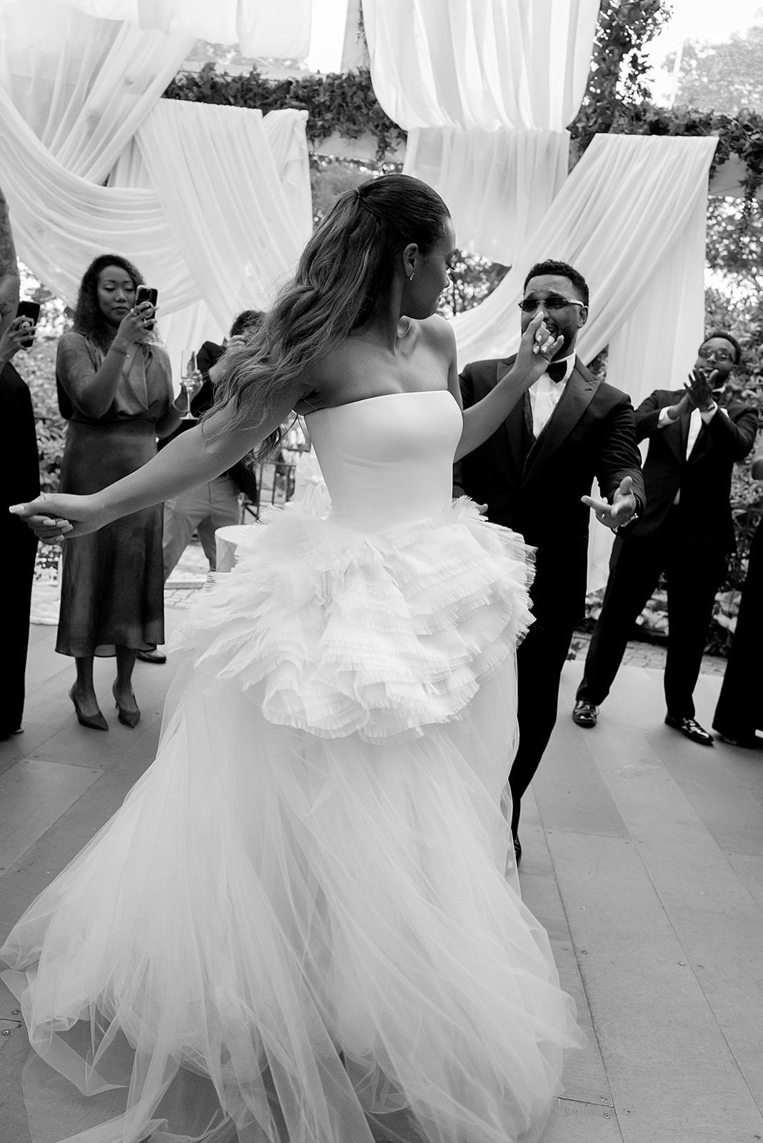 Black and white photograph of a bride dancing in a ruffled tulle gown.