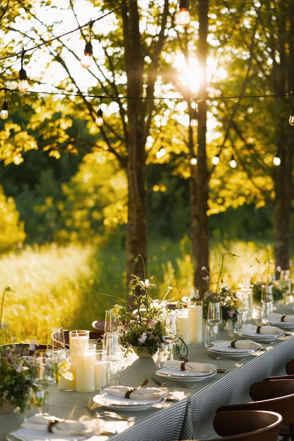Rustic golden-hour reception table with candles and wildflowers under string lights.
