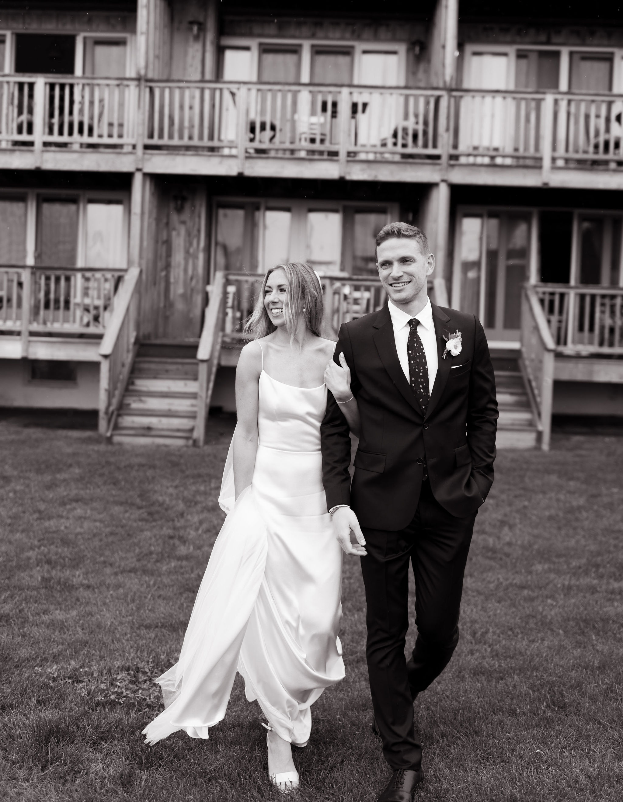 Black and white photograph of a couple walking arm-in-arm in front of a lodge.