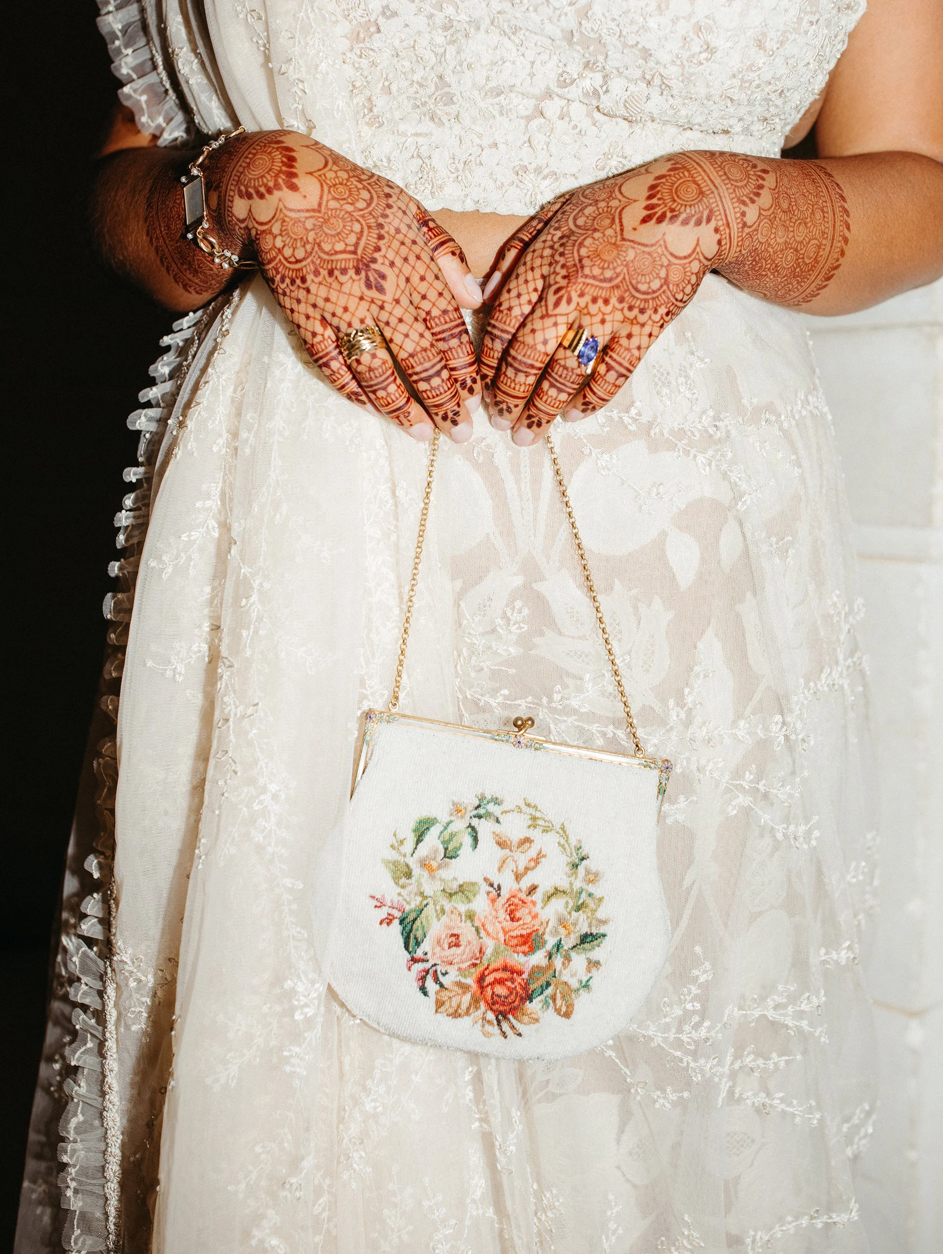 Bride's henna'd hands holding an embroidered floral clutch.