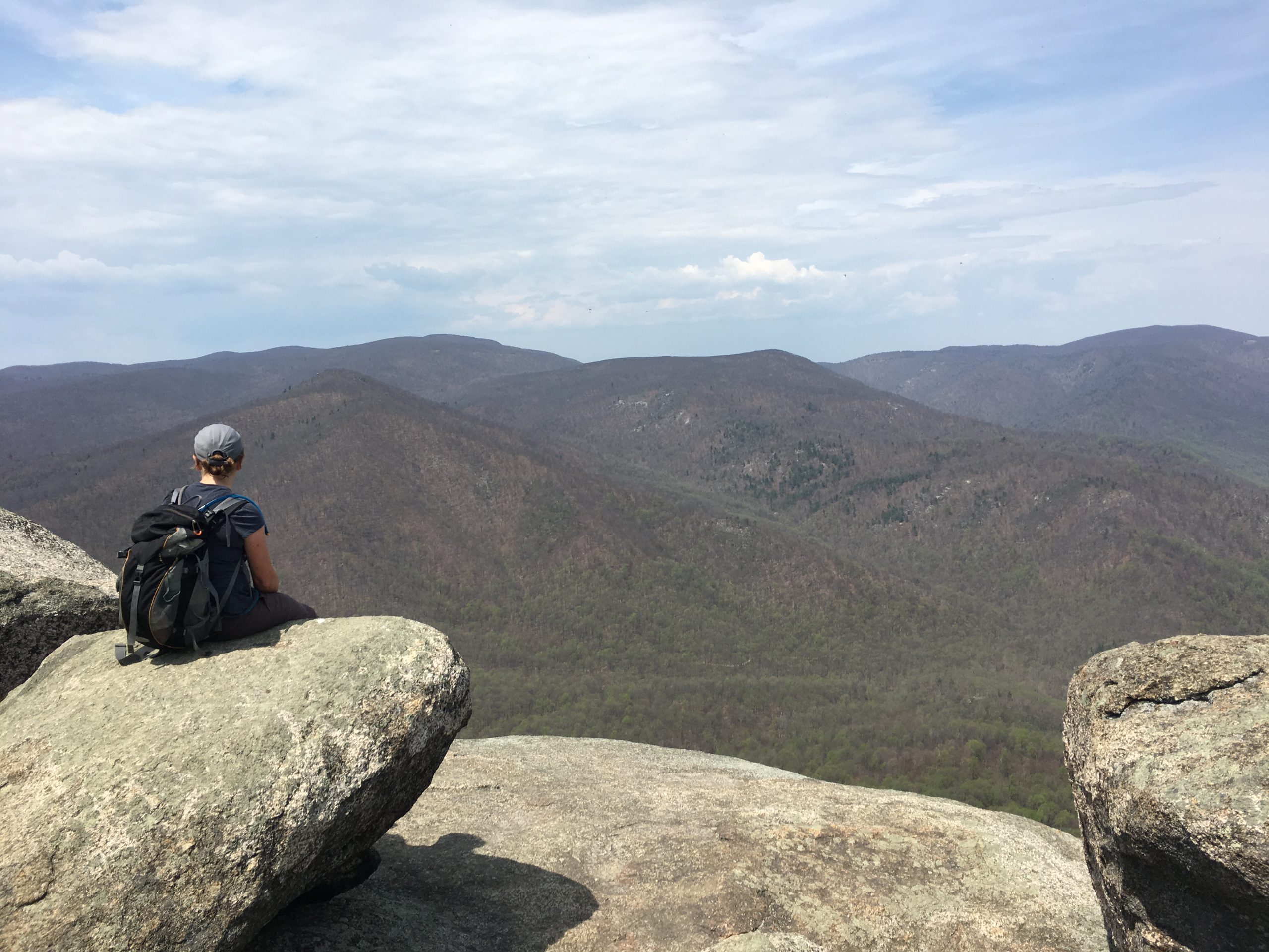 A backpacker sitting on a rocky outcrop overlooking a vast mountain valley