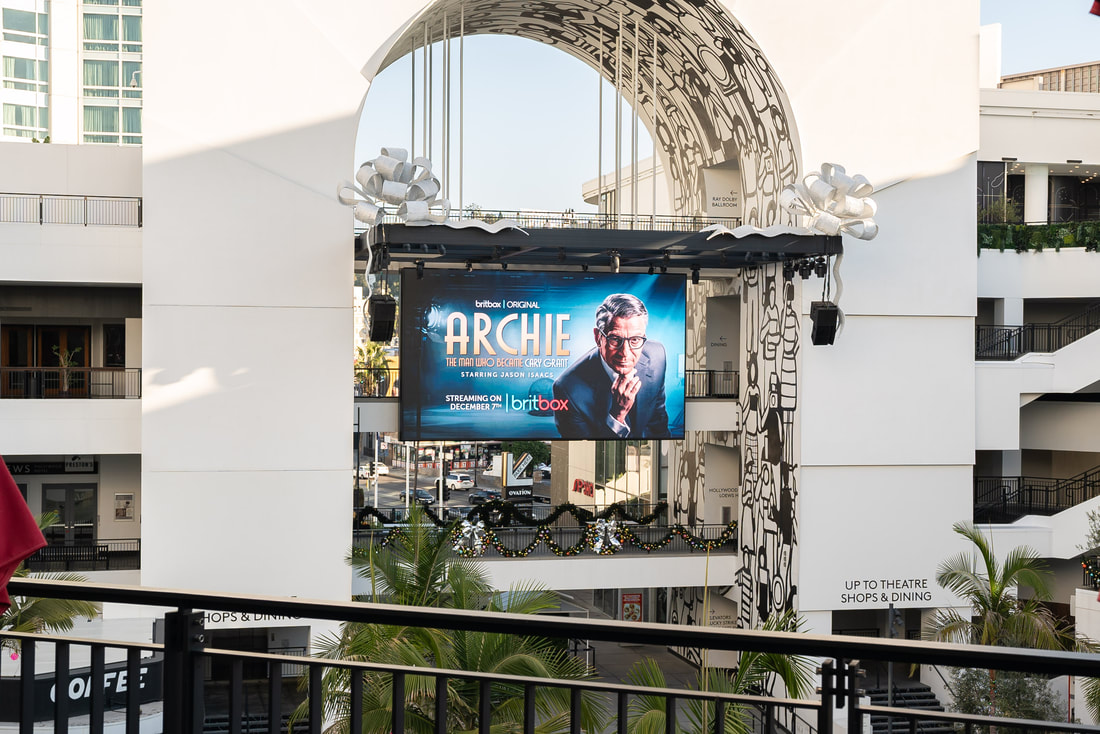 BritBox 'Archie' large screen at Ovation Hollywood viewed through decorative arch