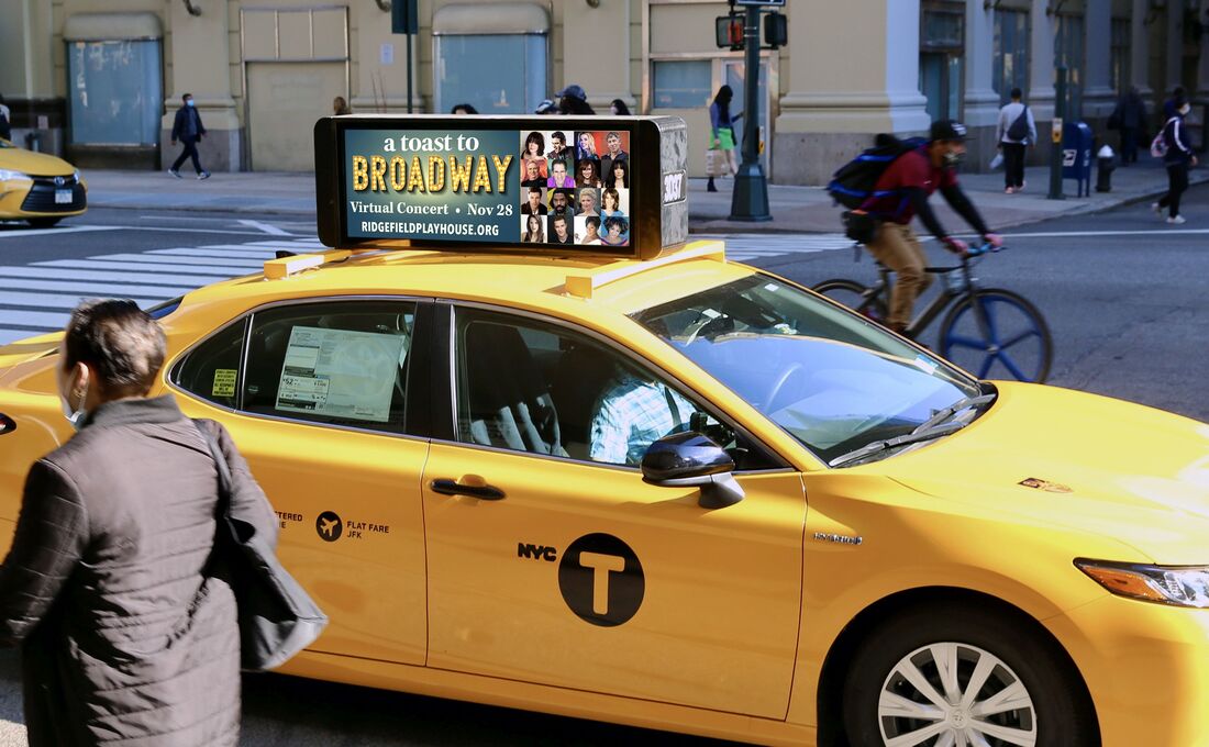 NYC yellow taxi with 'A Toast to Broadway' roof-top screen ad at a city intersection