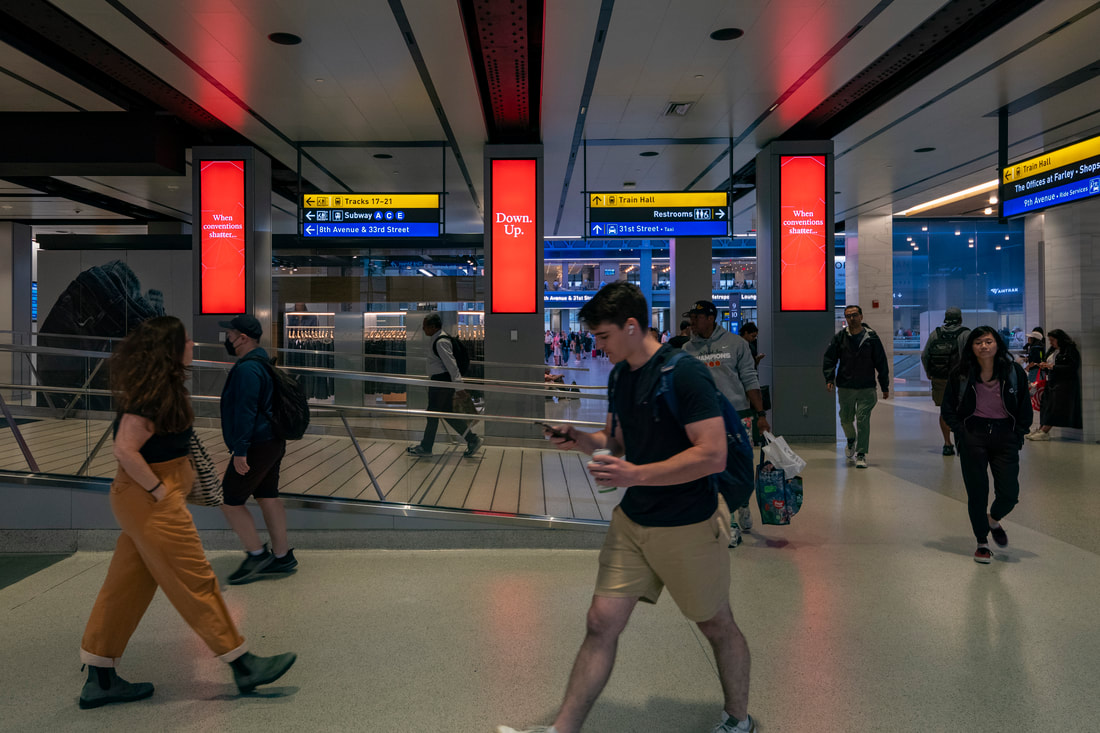 The Economist red vertical column screens in Moynihan Train Hall, Penn Station NYC