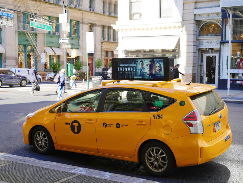 NYC yellow taxi with BritBox 'Sherwood' digital rooftop screen, SoHo street