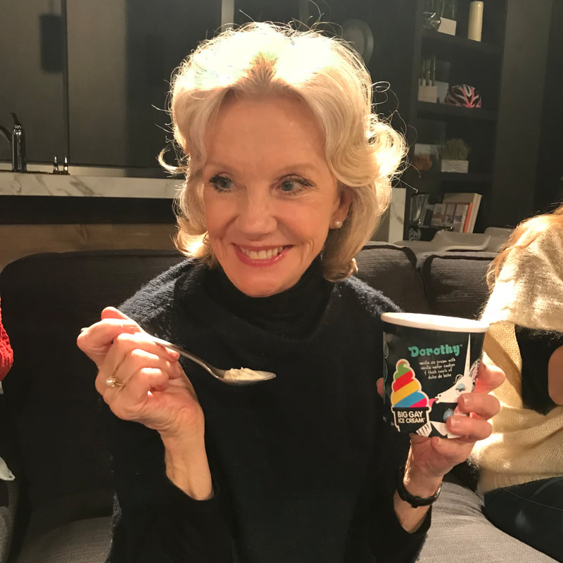 Blonde woman holding a Big Gay Ice Cream cup and spoon, smiling at camera indoors