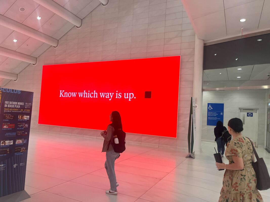 The Economist 'Know which way is up.' red digital screen inside Oculus WTC with passersby