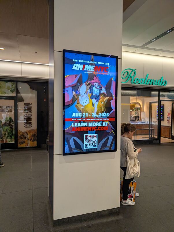 Anime NYC 2025 convention digital screen on a mall column, woman standing nearby