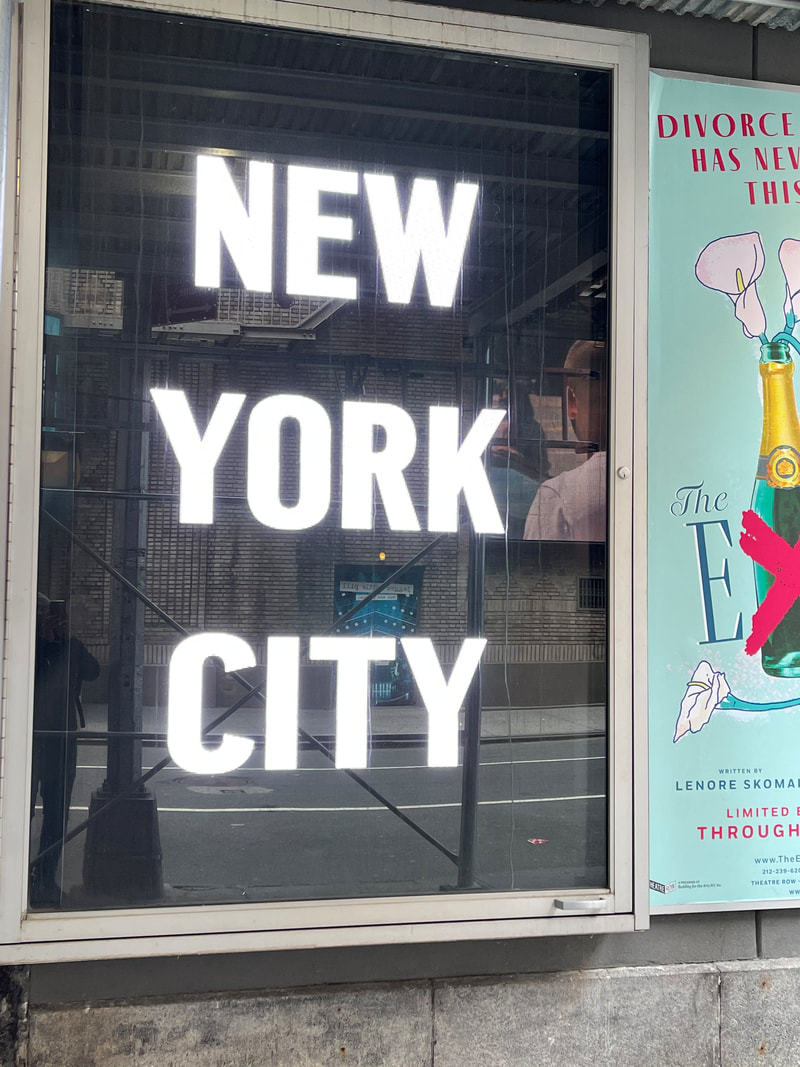 Illuminated 'NEW YORK CITY' letters in a bus shelter display case with a Broadway poster