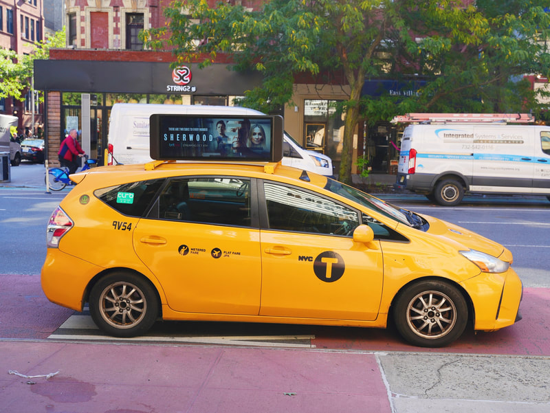 NYC yellow taxi with BritBox 'Sherwood' digital rooftop screen ad, East Village street