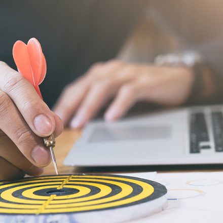 A hand placing a dart on a bullseye target next to a laptop