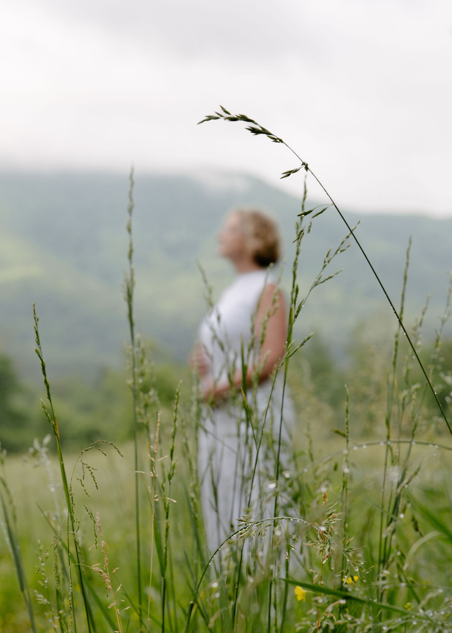 A woman in white standing in a green meadow seen through tall grasses
