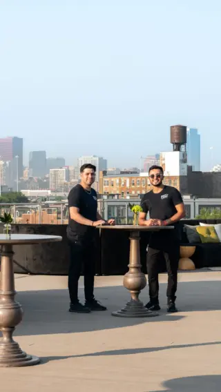 Two guests at a pedestal cocktail table on a rooftop with city skyline