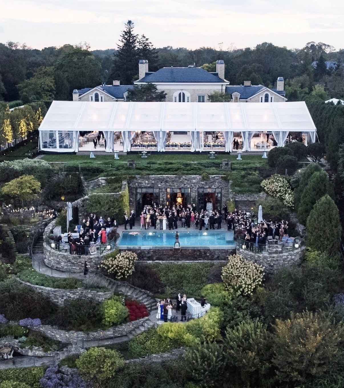Aerial view of a luxury estate wedding with a white marquee tent and pool at dusk