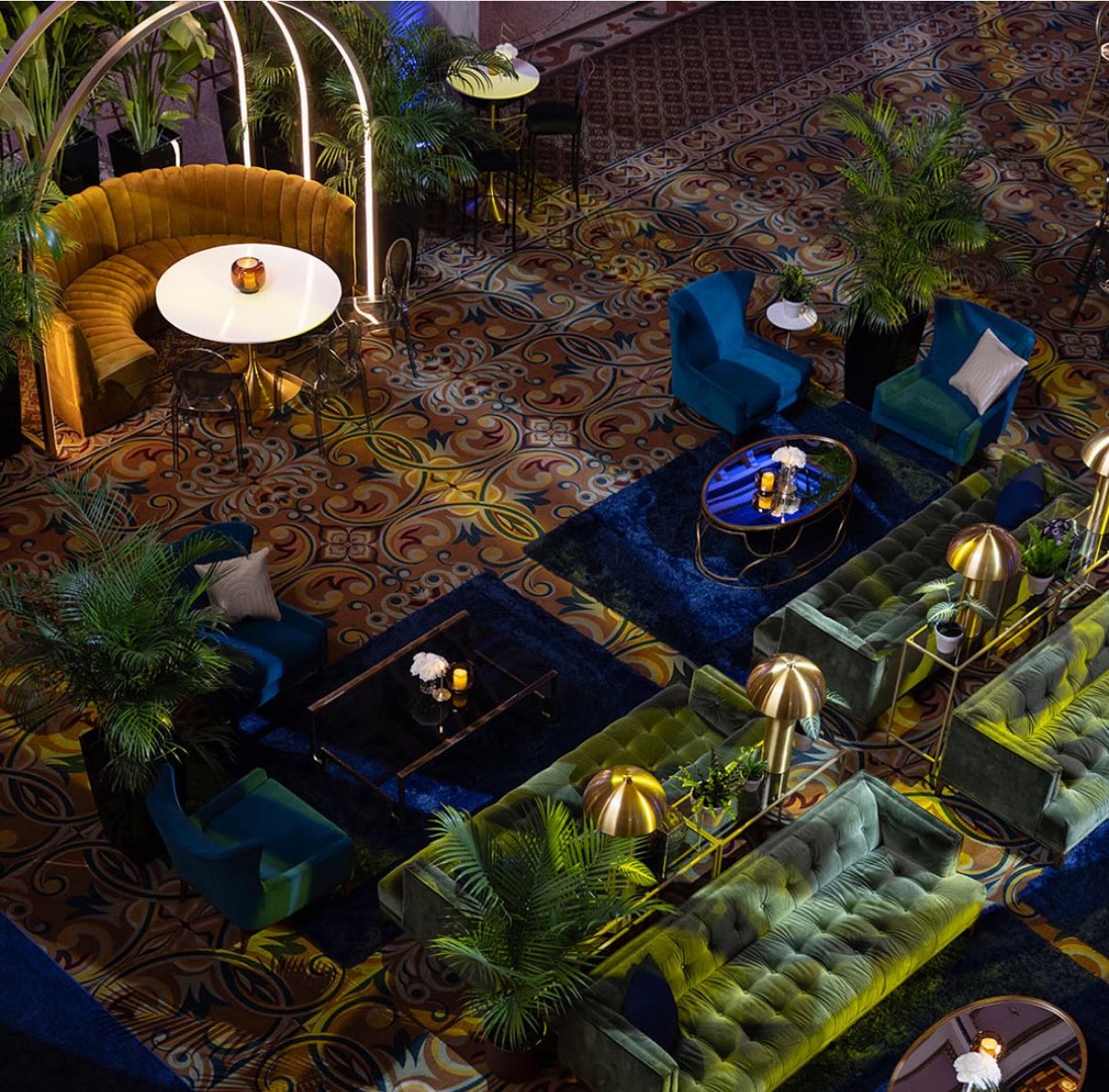Overhead view of an opulent event lounge with velvet sofas, tropical plants and patterned carpet