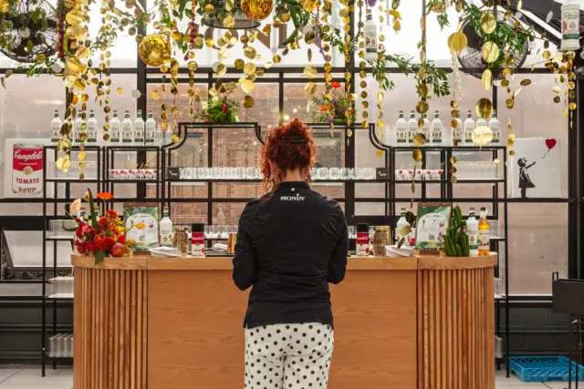 Branded cocktail bar station with a gold disc backdrop and floral ceiling decorations