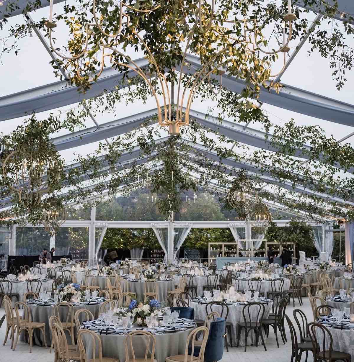 Clear-span wedding tent interior with round tables, bentwood chairs and greenery chandeliers