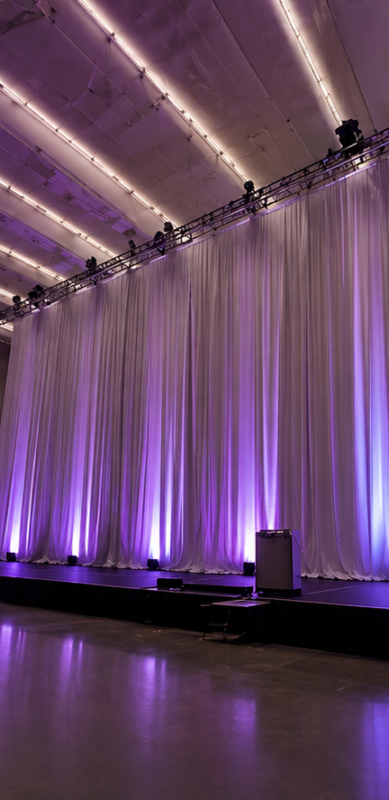 Tall white acoustic drape panels with purple uplighting in an event hall