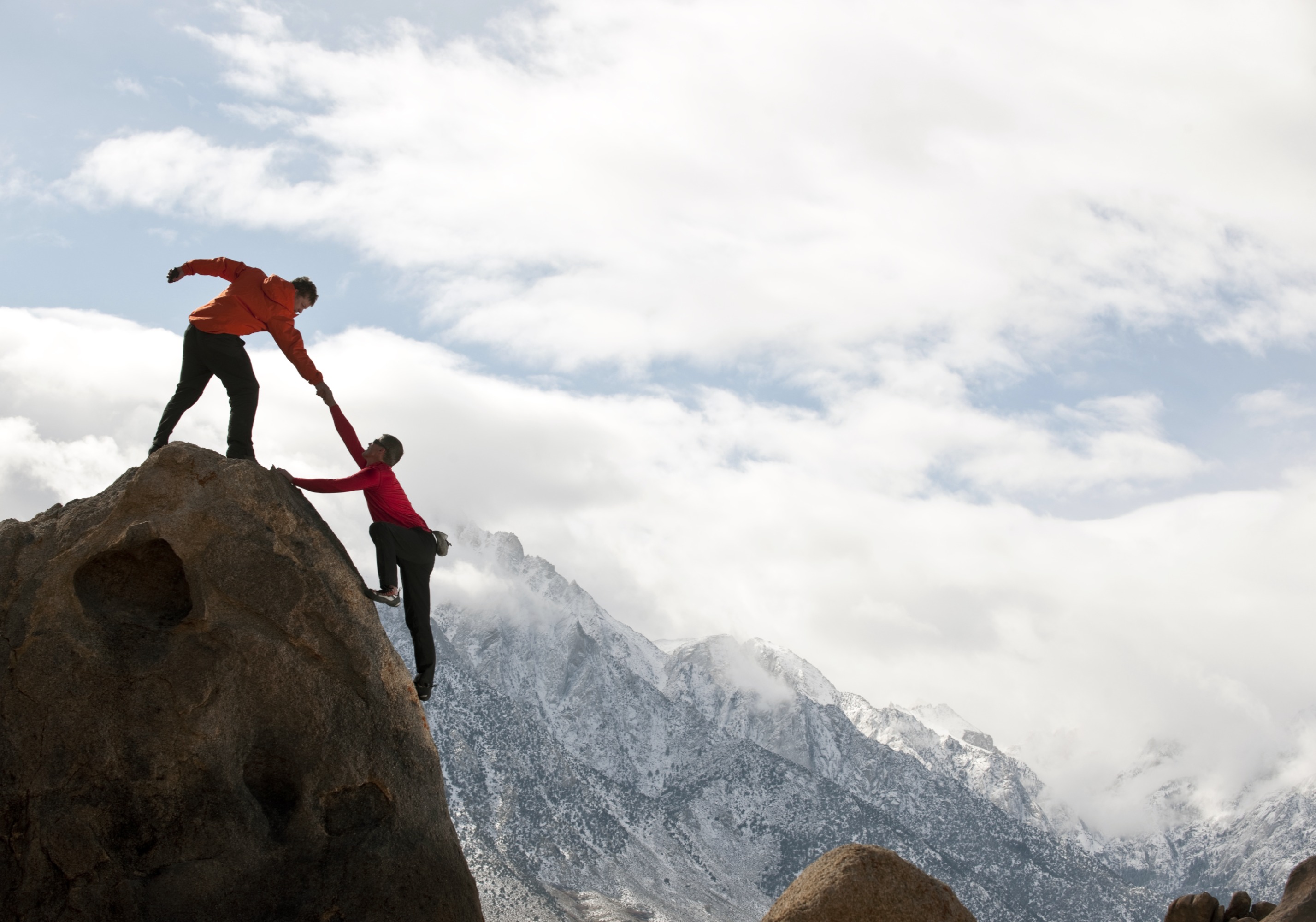 One climber pulling another up a rock face on a mountain summit