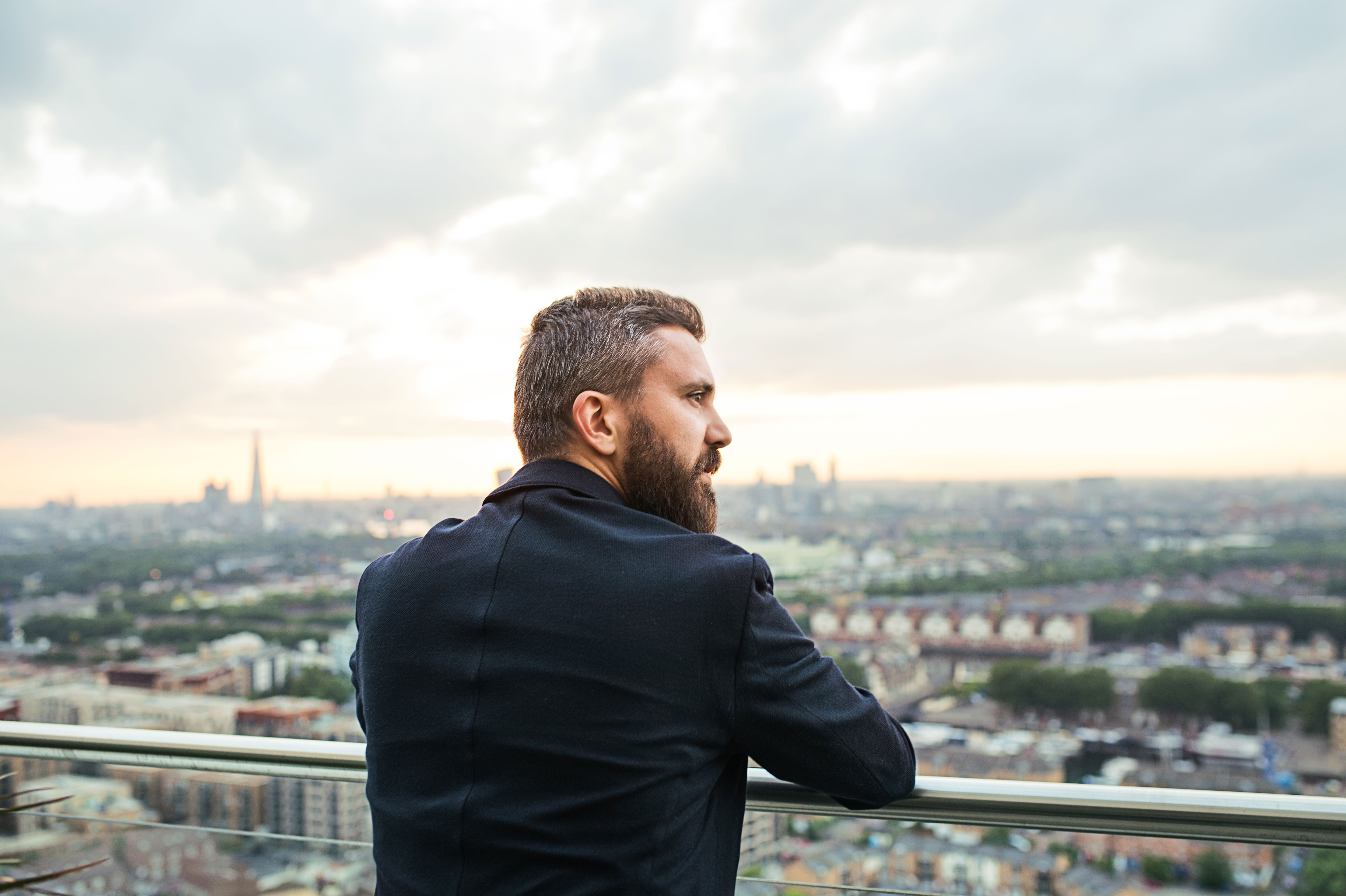 A man looking out over a city skyline at sunset from a rooftop