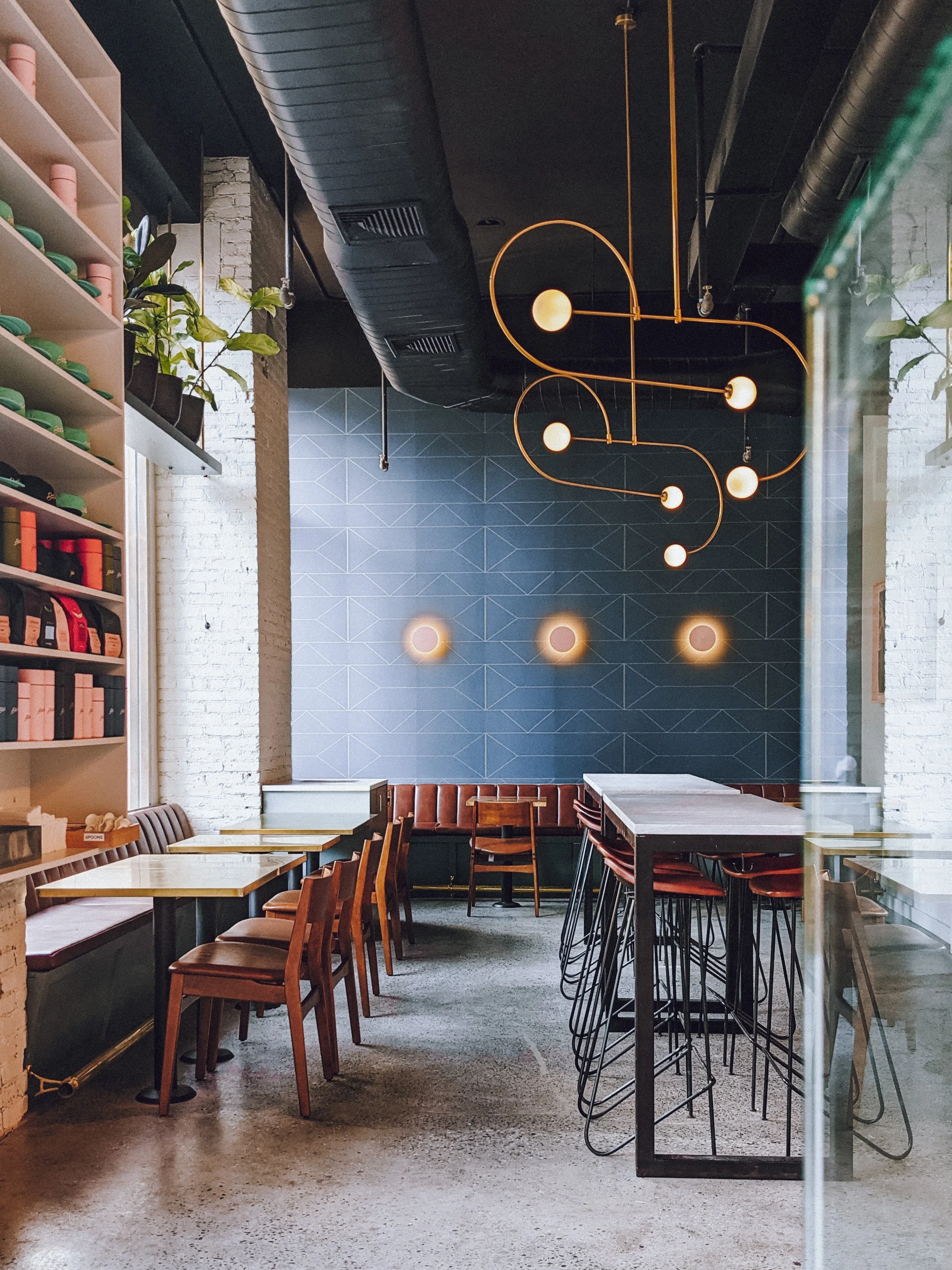 Butler interior with blue accent tile wall, brass chandelier, bar stools and a retail shelf