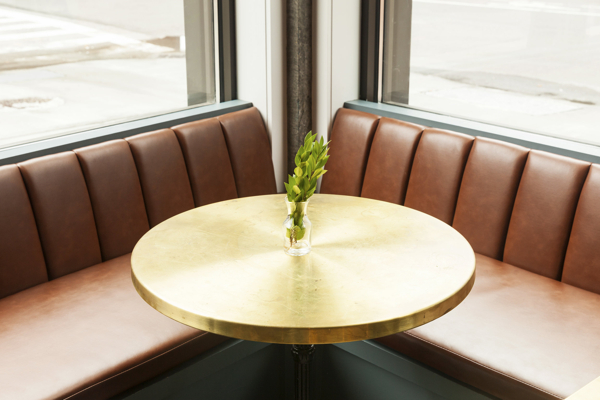 Corner booth with a brass round table and small plant, street view through the window