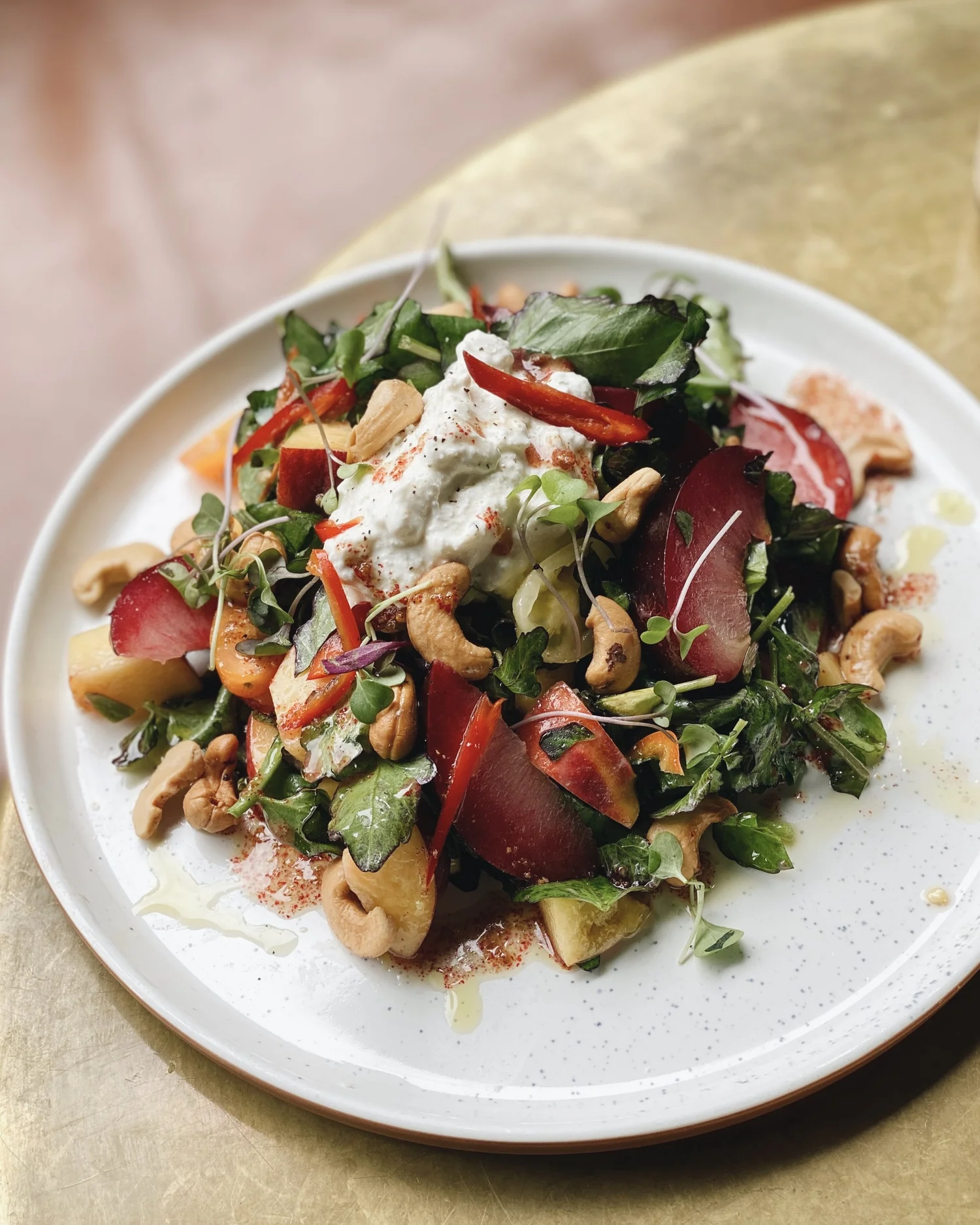 Stone fruit and cashew salad with burrata on a white speckled plate
