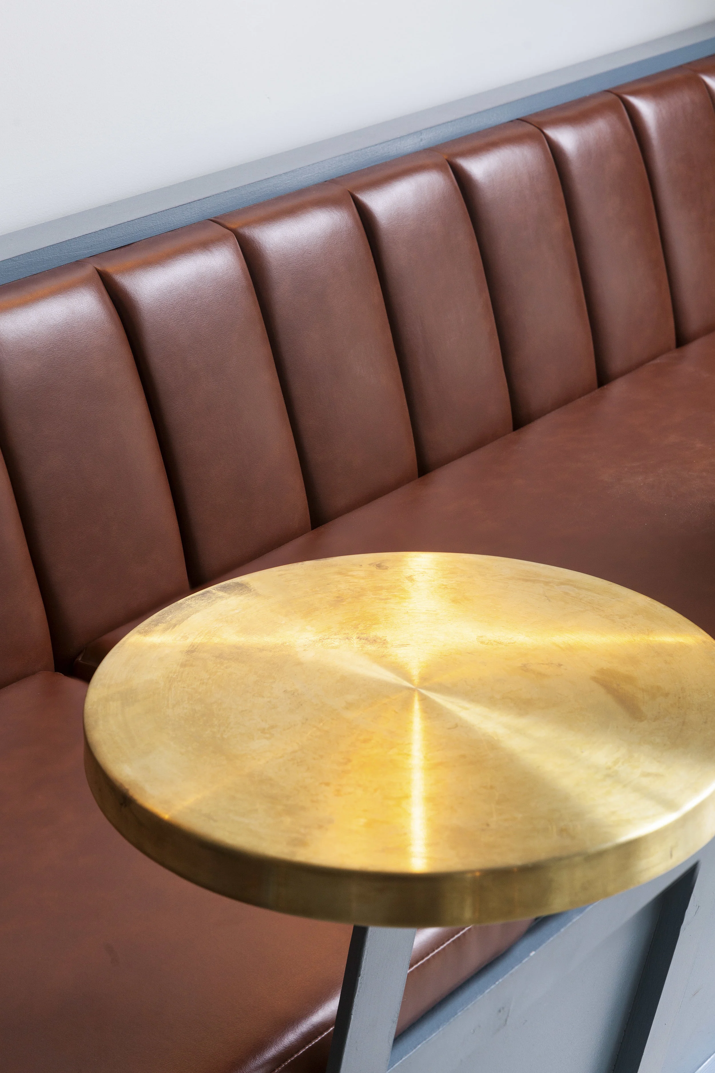 Brown leather channel-tufted banquette with a round brass table