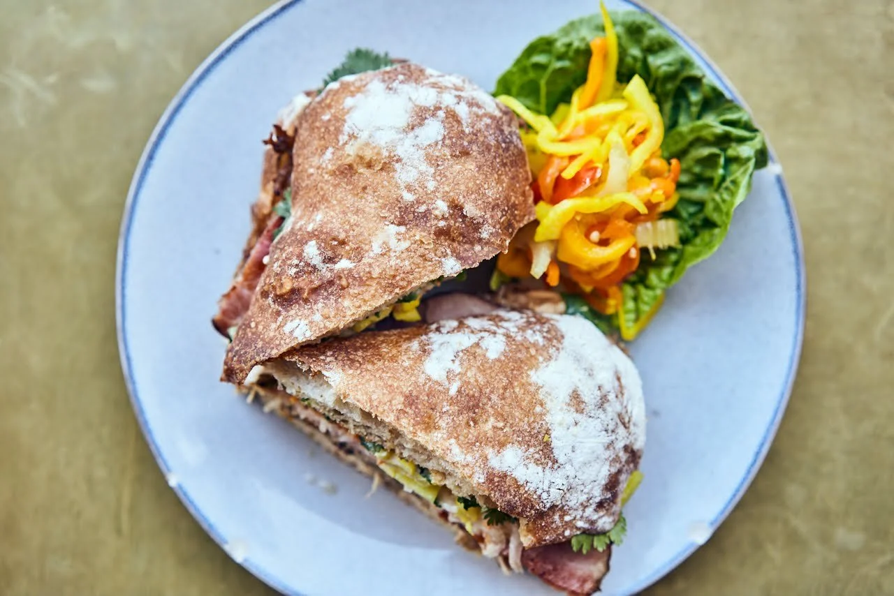 Rustic ciabatta sandwich halved on a pale blue plate with pickled peppers and greens
