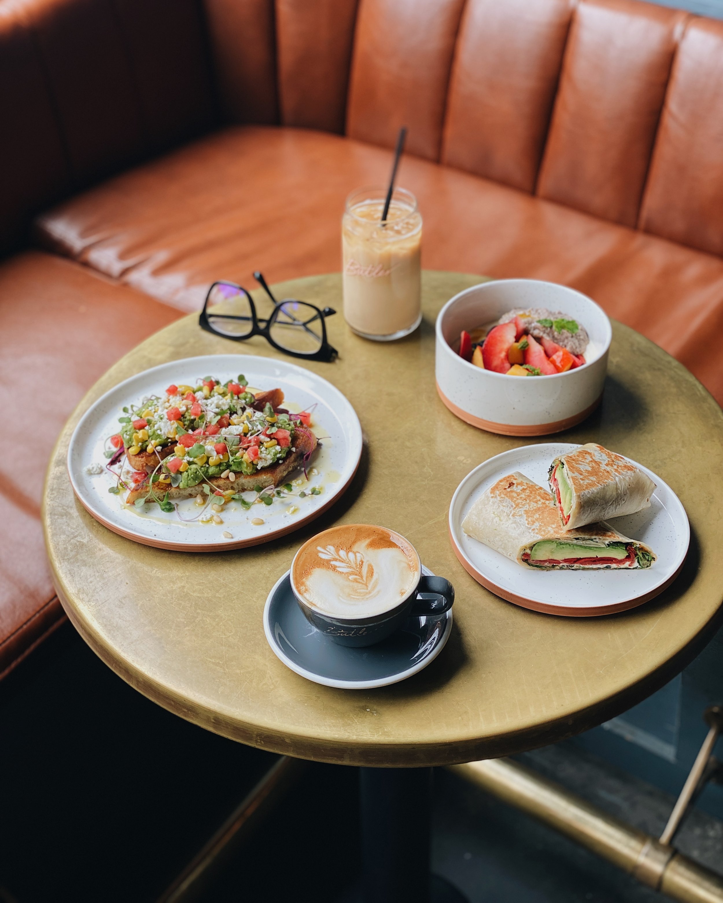 Multiple dishes and drinks on a brass table against a leather banquette