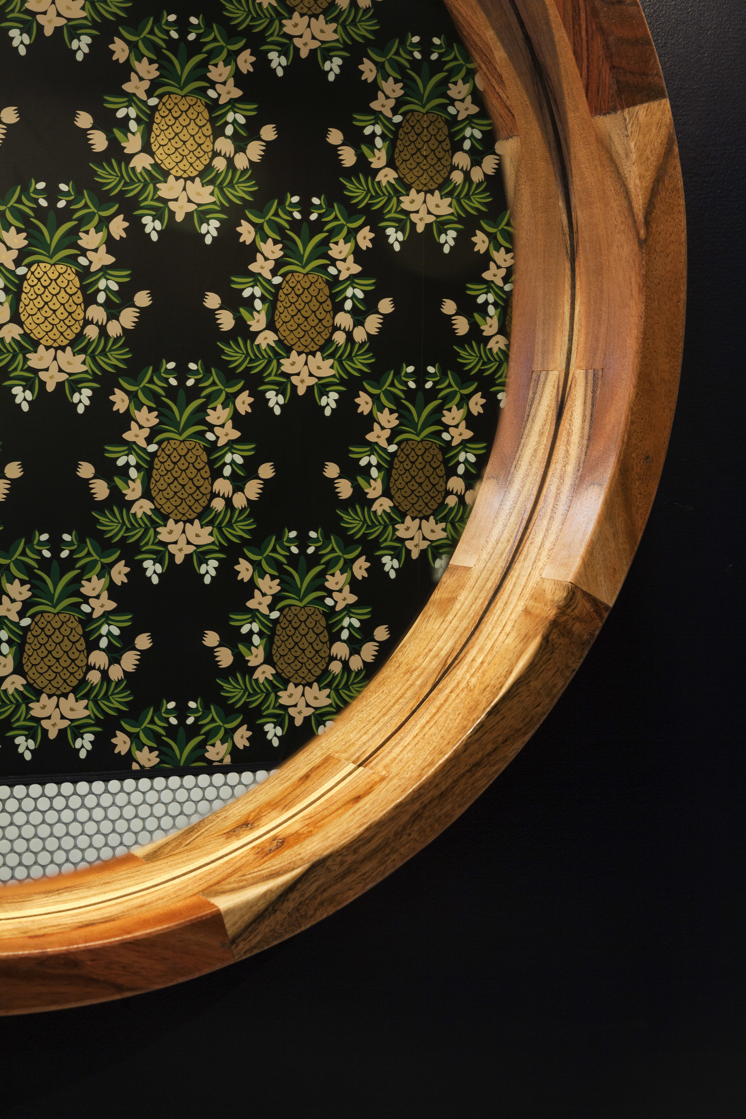 Pineapple-pattern wall mural framed by a circular wood surround above penny tile
