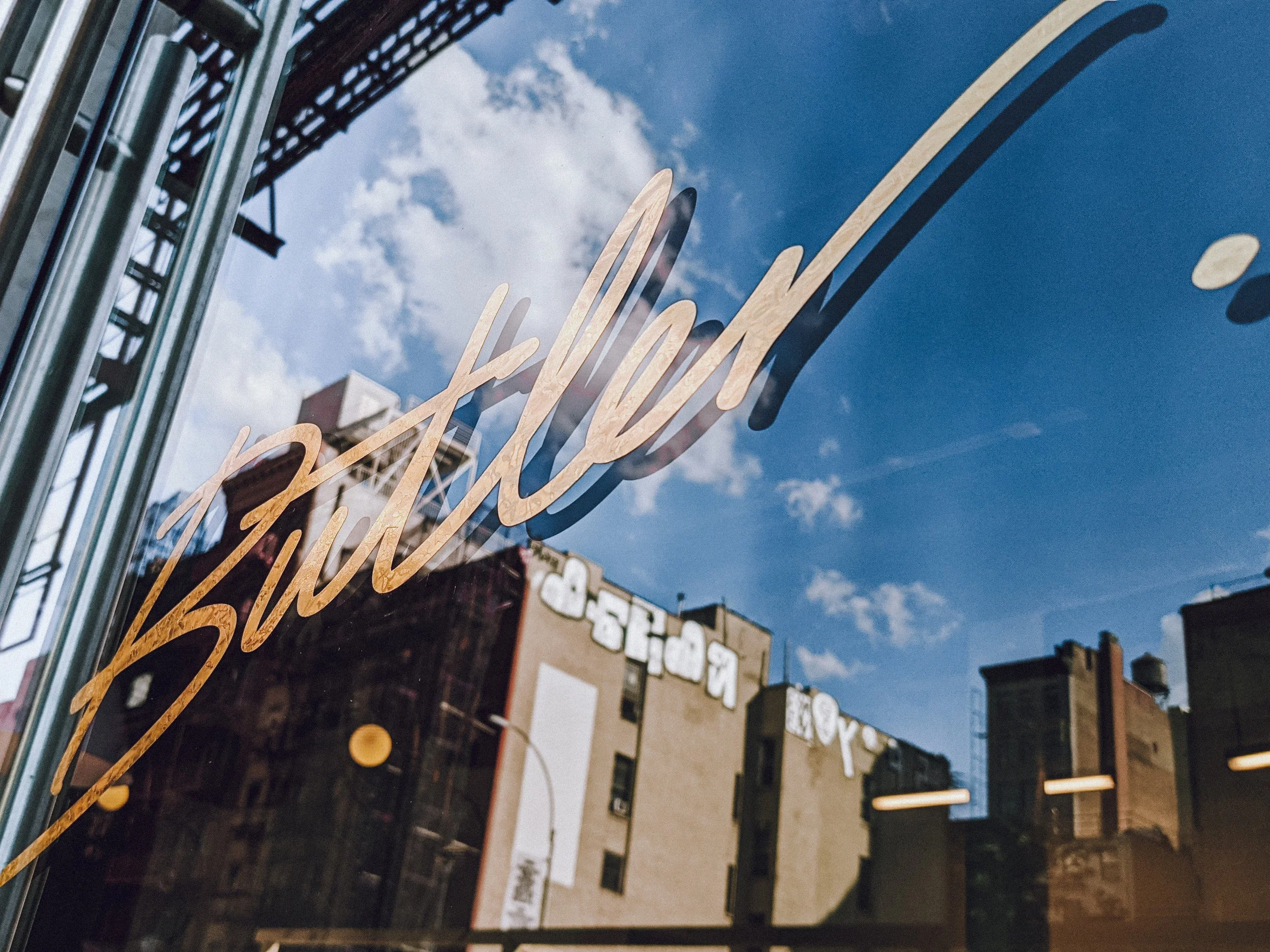 Gold Butler script decal on the shop window with the Brooklyn skyline reflected in the glass