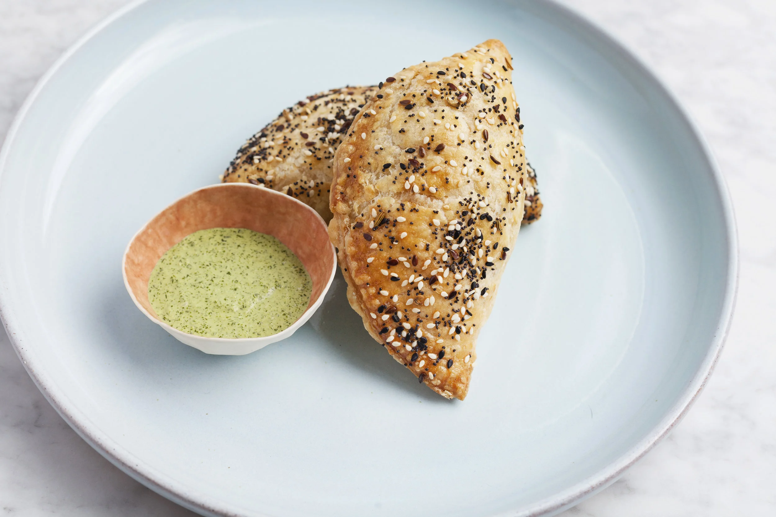 Seeded empanada with green herb dipping sauce on a pale blue plate