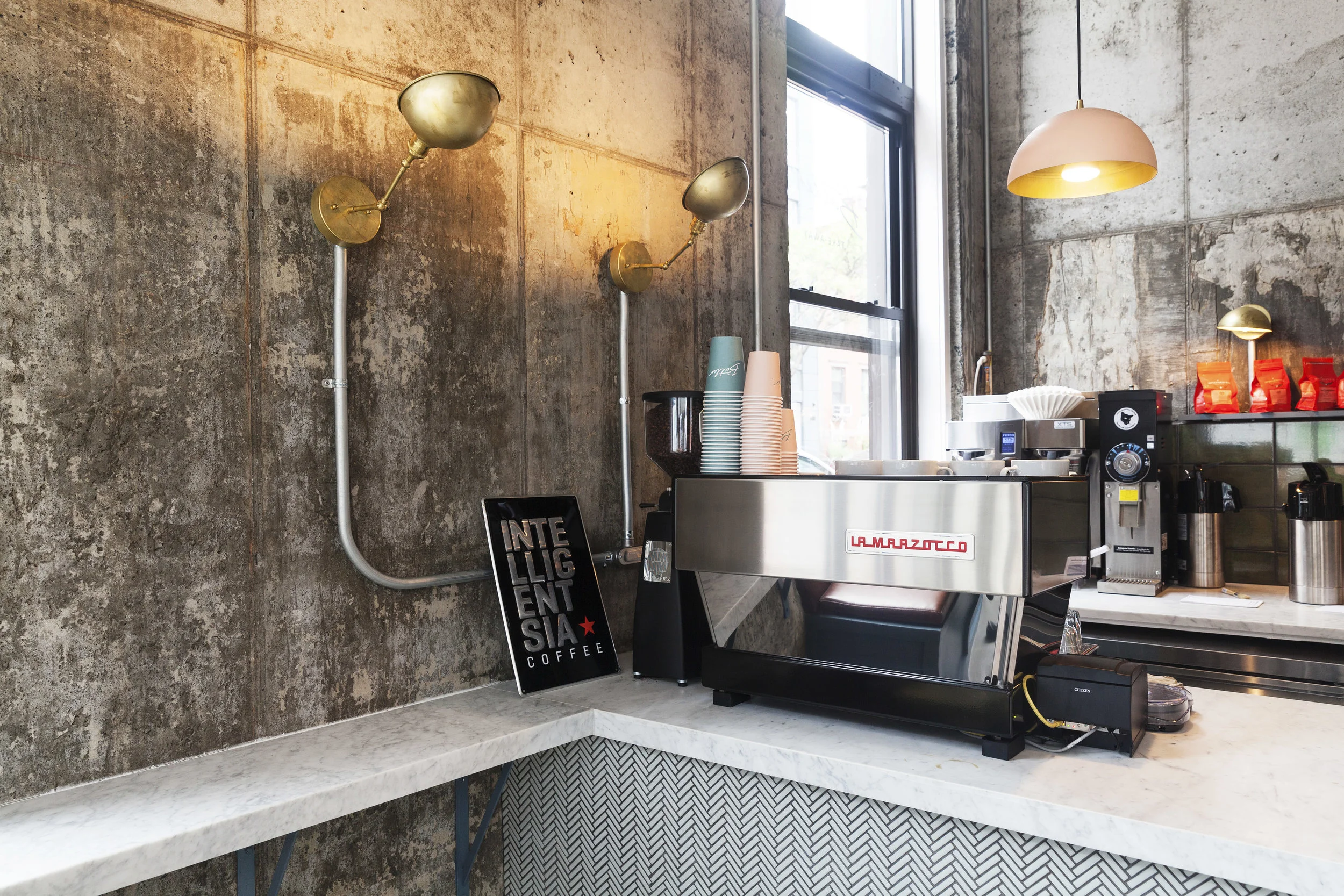 La Marzocco espresso machine on a marble corner counter with Intelligentsia sign and brass sconces