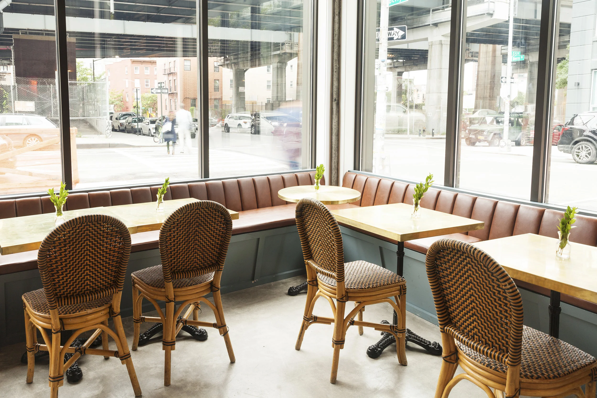 Window-side seating with rattan bistro chairs, brass tables and a leather banquette