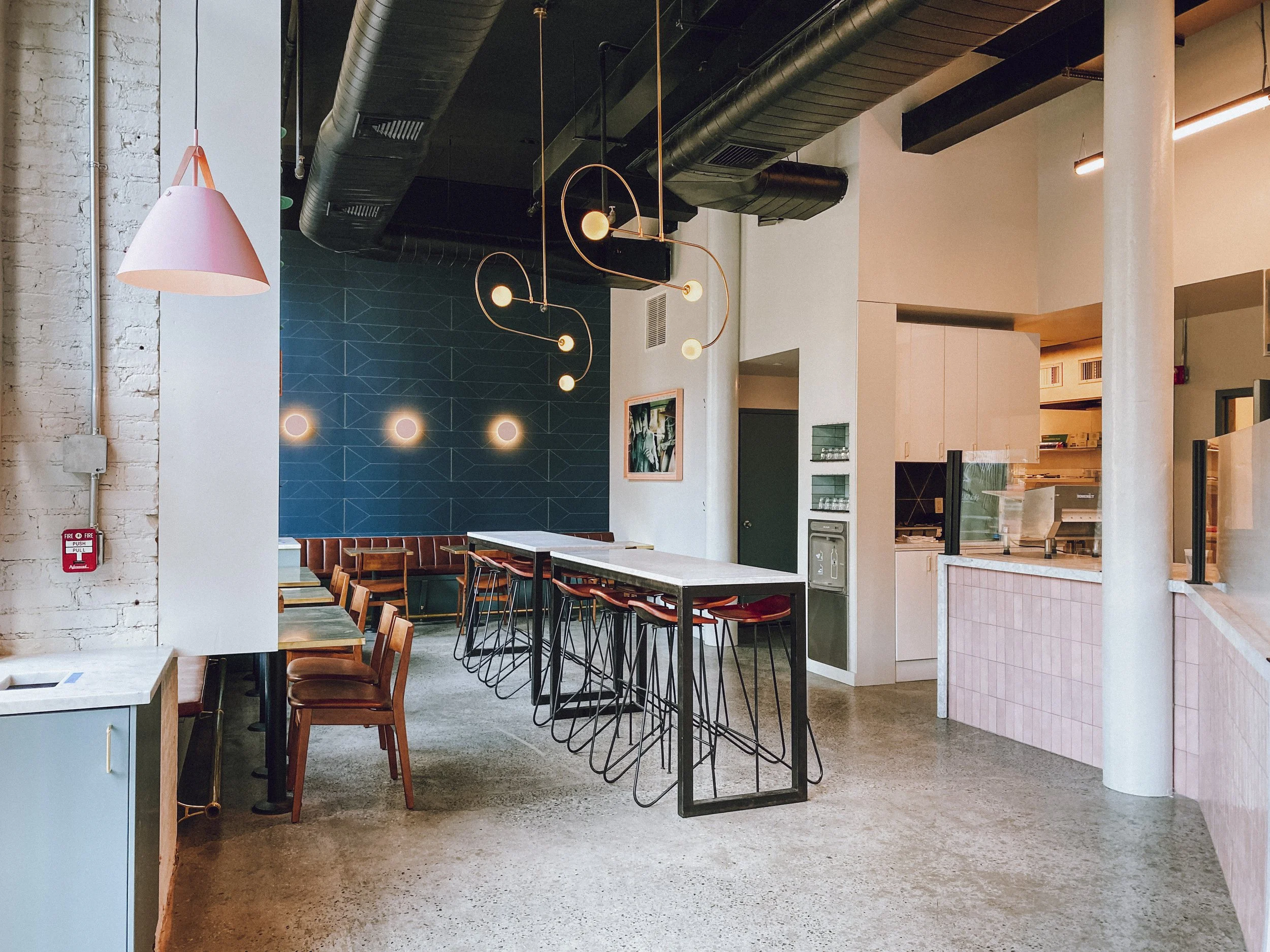 Wide interior with communal marble bar, blue tile wall, pink pendant and open kitchen