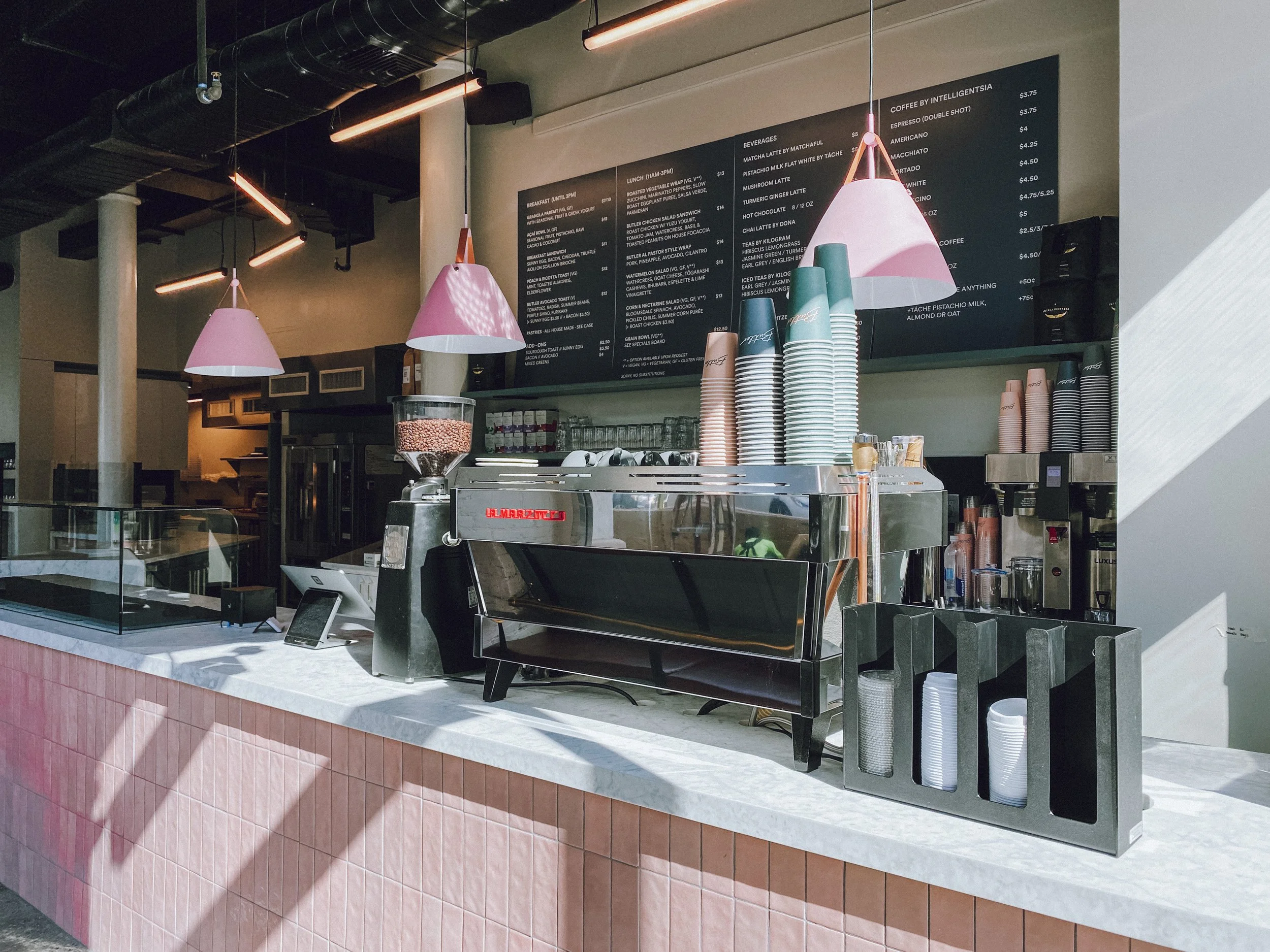 Coffee bar counter with pink tile, La Marzocco machine, pink pendants and black menu board