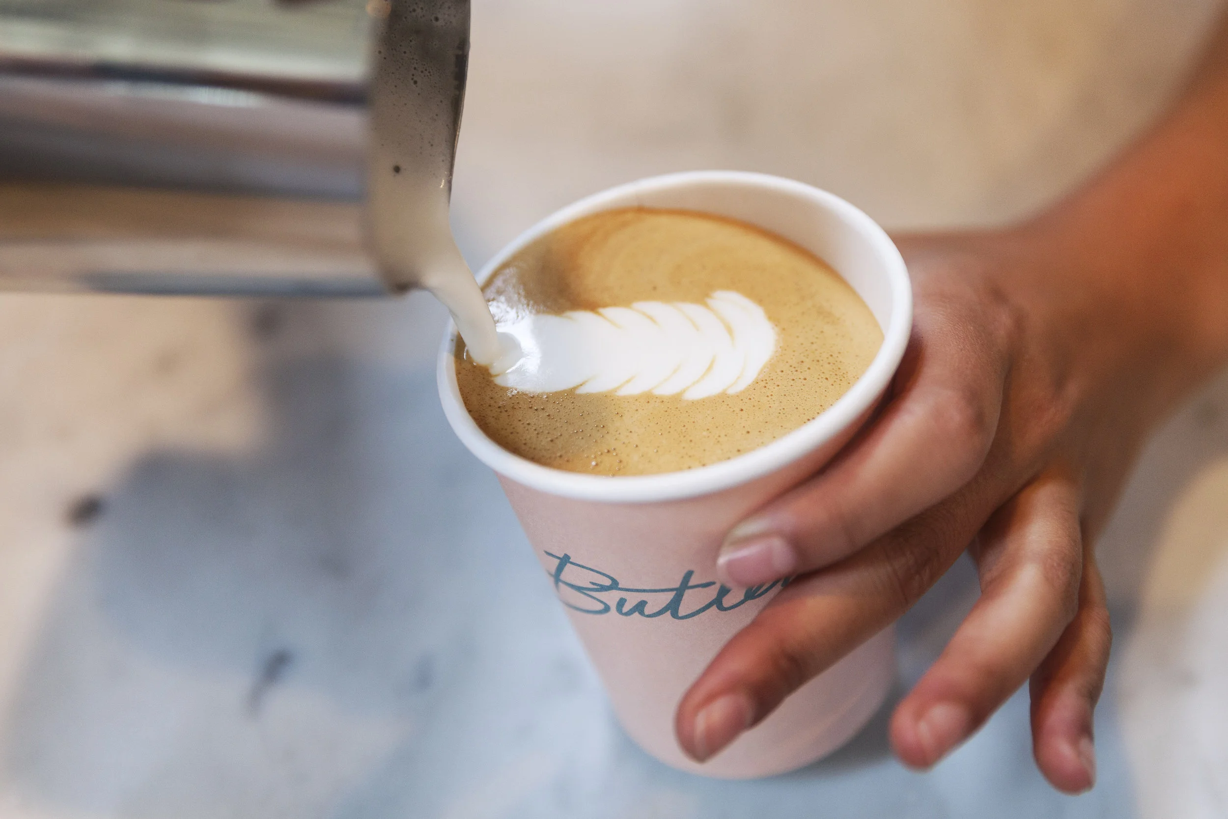 Barista pouring steamed milk into a Butler-branded pink cup
