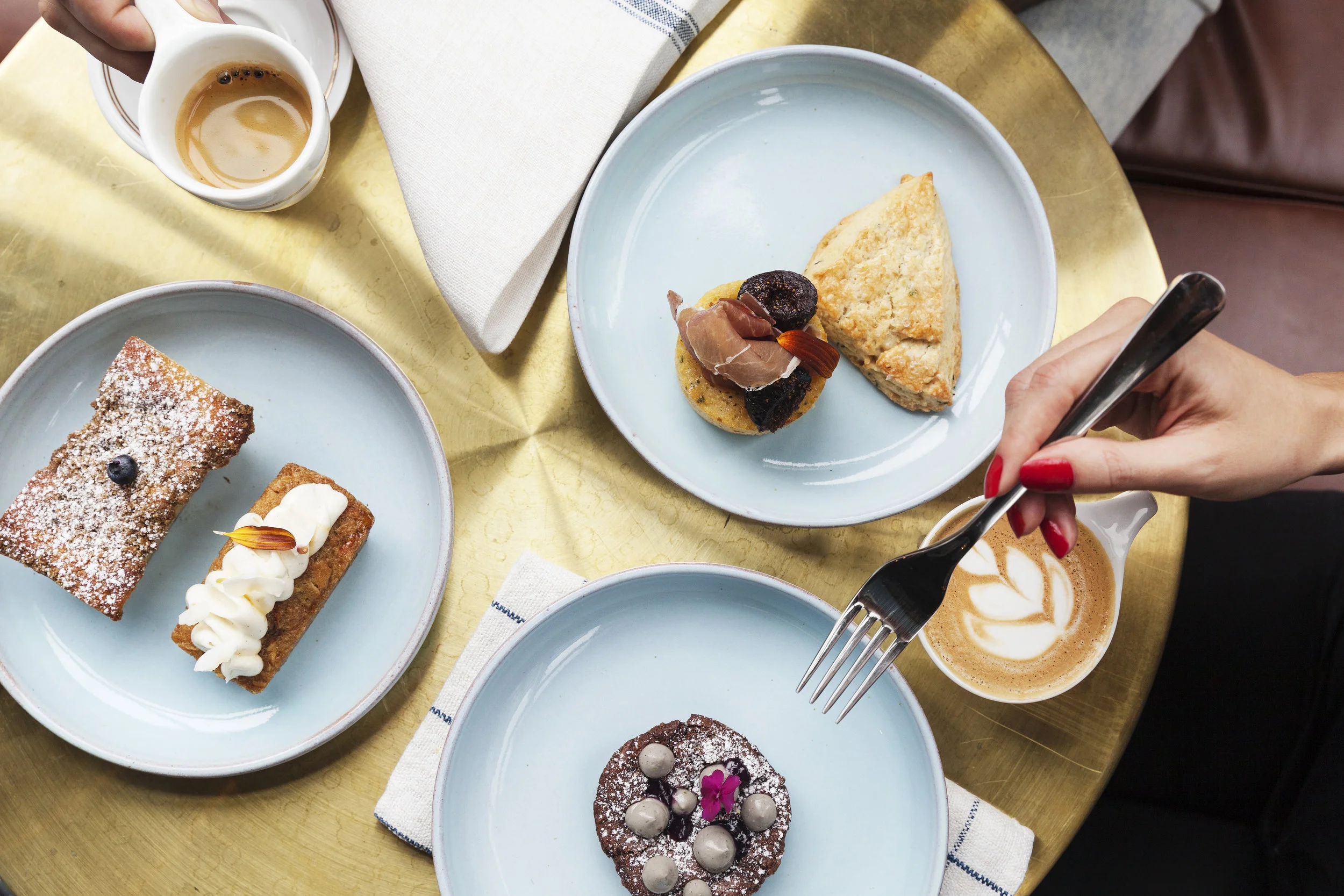 Overhead pastry spread — babka, chocolate brownie, scone and fig muffin — on pale blue plates